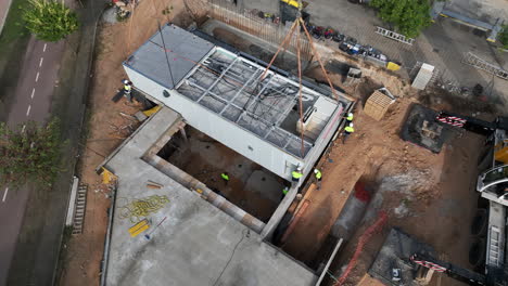 Aerial-view-looking-down-at-construction-crew-lifting-modular-housing-unit-into-real-estate-foundation