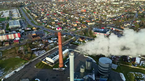 Smokestack-spewing-steam,-smoke-and-pollution-in-a-city---aerial-orbit
