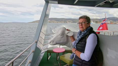 Hobart,-Tasmania,-Australia---13-March-2019:-Woman-passenger-admiring-the-view-on-a-tourist-boat-leaning-against-a-life-sized-model-of-a-cow