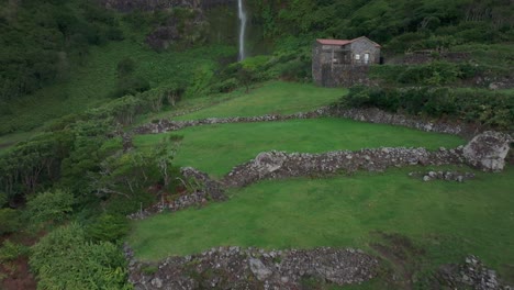 Reveal-aerial-shot-of-cascata-do-poço-do-bacalhau-waterfall-with-house