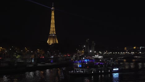 Beleuchteter-Eiffelturm-Bei-Nacht-Mit-Fähren,-Die-Die-Seine-überqueren-Und-Die-Stadt-Paris-überblicken