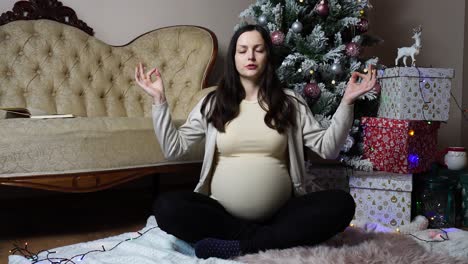 Mujer-Embarazada-Hace-Pose-De-Meditación-De-Yoga-Cerca-Del-árbol-De-Navidad-Y-Regalos.