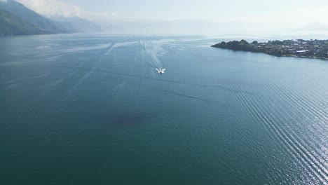 Vista-De-Drones-En-Guatemala-Volando-Sobre-Un-Bote-En-Un-Lago-Azul-Con-Montañas-Verdes-Al-Costado-En-Un-Día-Soleado-En-Atitlán