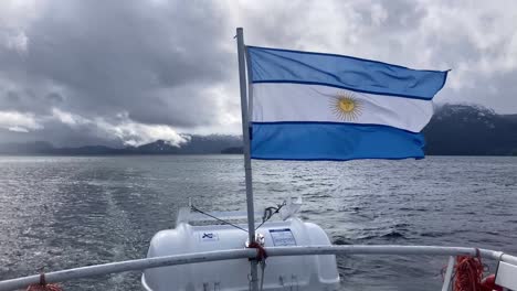 Argentine-flag-waving-on-ferry-in-Nahuel-Huapi-lake,-Villa-La-Angostura,-wide-shot