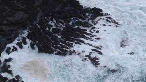 Top-down-view-of-rough-sea-waves-hitting-rocky-coastline,-aerial