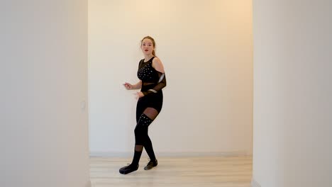 Young-attractive-female-dancer-performing-a-slow-motion-dance-inside-home-wearing-a-black-outfit-in-front-of-the-white-wall