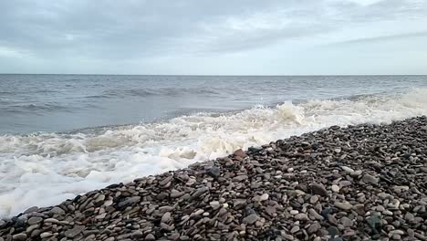 Sandy-waves-slow-motion-crash-onto-Welsh-pebble-beach