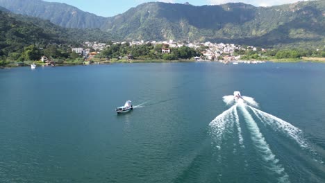 Drone-view-in-Guatemala-flying-over-boats-on-a-blue-lake-with-green-mountains-and-volcanos-on-a-sunny-day-in-Atitlan