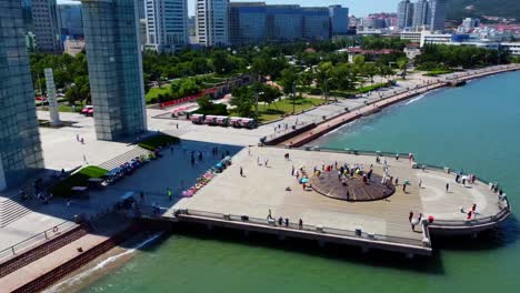 Aerial-view-of-Weihai-Xingfu-Park-pier-with-people-standing-on-monument-with-ancient-writings,-China