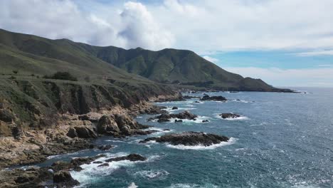 Waves-crash-into-the-cliffs-with-mountain-views-in-the-back-ground-near-Big-Sur,-California