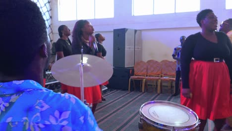 Black-vocalist-woman-singing-with-microphone-while-another-guy-plays-the-drums