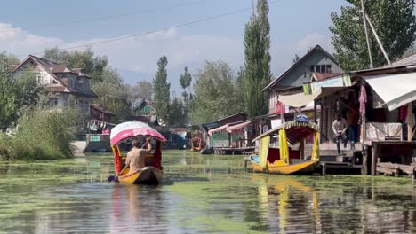 Dal-Lake-Kashmiri,-Un-Hermano-Conduce-Un-Bote-Entre-Casas-Y-Mucha-Gente-Lo-Observa