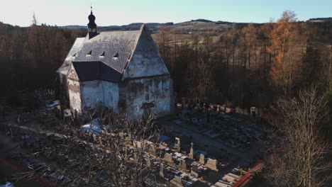 Aerial-view-of-a-gothic-church-surrounded-by-graves-in-the-Šumava-landscape-of-Velhartice