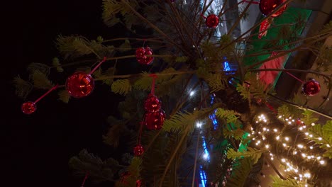 Glänzende-Weihnachtsdekorationen-Und-Helle-Lichter-Schmücken-Einen-Weihnachtsbaum-Vor-Einem-Gebäude-In-Einer-Südostasiatischen-Stadt