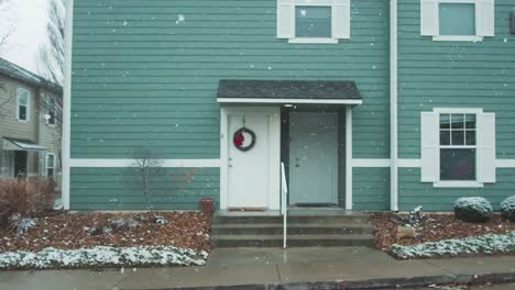 A-cinematic-scene-captures-the-snow-in-slow-motion-within-a-residential-setting,-a-street-adorned-with-a-staircase-leading-to-a-building-entrance,-set-against-a-somber-and-overcast-weather-backdrop
