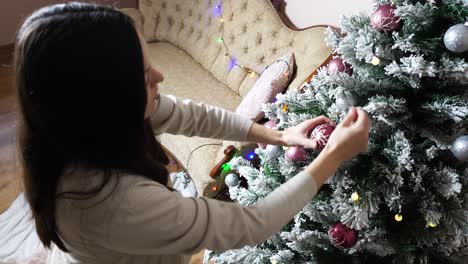 Pregnant-woman-add-decorations-on-green-indoor-artificial-Christmas-tree