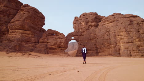 Hombre-Caminando-Cerca-De-Una-Roca-Con-Forma-De-Elefante-Al-Atardecer-En-El-Parque-Nacional-Tassili-N&#39;ajjer,-Argelia---Disparo-De-Un-Dron
