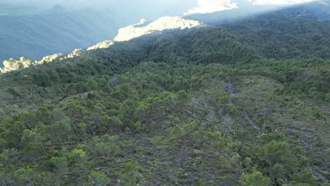 Drone-view-in-Guatemala-flying-over-a-volcano-mountain-covered-by-green-trees-at-sunrise-surrounded-by-green-mountains