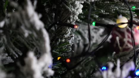 Close-up-of-twinkle-light-garland-on-artificial-Christmas-tree,-snow-imitation