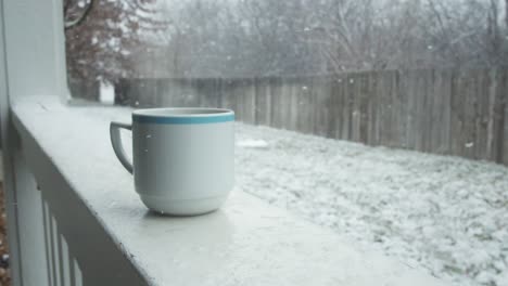 A-mug-of-hot-chocolate-rests-in-the-snow-on-the-balcony-porch,-overlooking-the-backyard-of-the-house