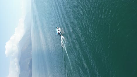 Drone-portrait-view-in-Guatemala-circling-around-a-boat-over-a-blue-lake-surrounded-by-green-mountains-and-volcanos-on-a-sunny-day-in-Atitlan