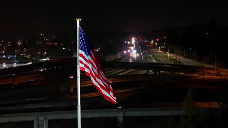 Amerikanische-Flagge-Mit-Autos,-Die-Nachts-über-Die-Autobahn-Im-Hintergrund-Fahren