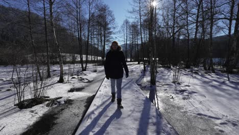 Hombre-Caminando-Emociona-Sobre-Un-Puente-Nevado-En-Un-Bosque-De-Paisaje-Invernal