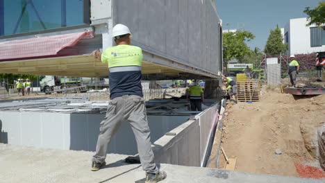 Construction-contractor-workman-guiding-smart-modular-housing-unit-slow-motion-onto-foundation