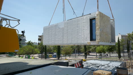 Modular-housing-unit-suspended-from-crane-installing-into-construction-site-foundation