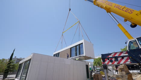 Modular-housing-unit-hanging-from-crane-placed-into-position-on-construction-site