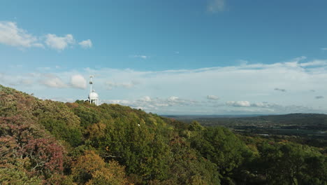 Flight-Above-Fall-Forest-On-Mountain-With-Water-Tank-And-Telecom-Tower-Atop