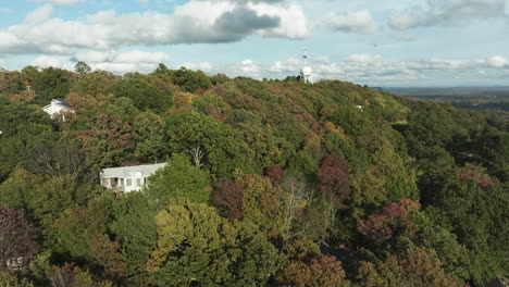 Flying-Over-Autumn-Woods-With-Water-Tank-Tower-In-The-Background-In-Fayetteville,-Mount-Sequoyah,-Arkansas,-USA
