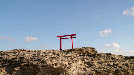 Vista-Minimalista-De-La-Puerta-Roja-Japonesa-Sobre-Rocas-Contra-El-Cielo-Azul