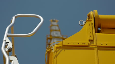Shallow-focus-looking-up-at-yellow-industrial-crane-boom-arm-under-blue-sky