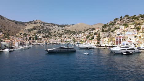 Drone-shot-of-a-large-luxury-yacht-leaving-the-port-of-Symi,-Greece