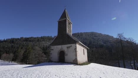 Wide-shot-of-scenic-Chapelle-St-Florent,-around-the-snow-covered-mountains-near-Longemer-lake