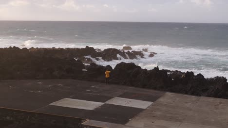 Man-yellow-jacket-standing-in-front-of-rough-sea-big-waves,-Azores-Portugal