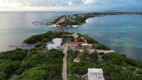 Drohnenansicht-In-Belize,-Die-An-Einem-Bewölkten-Tag-über-Das-Dunkel--Und-Hellblaue-Meer-Der-Karibik-Fliegt,-Einen-Weißen-Sandcaye,-Der-Mit-Palmen-Und-Restaurants-Bedeckt-Ist