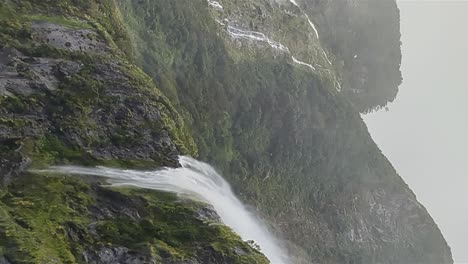 A-mass-of-water-flows-down-a-steep-cliff-during-a-heavy-rainstorm-in-Miford-Sound,-New-Zealand_vertical-shot