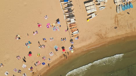 Drone-top-down-shot-capturing-beach-filled-with-swimmers-and-sunbathing-families,-creating-unforgettable-memories-during-the-summer-holidays