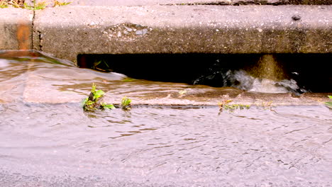 Fresh-rainwater-runoff-down-concrete-road-gutter-into-storm-drain,-close-up