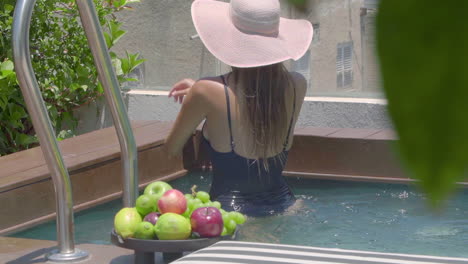 A-woman-in-a-black-bathing-suit-and-a-straw-hat-on-her-head-enjoys-in-a-private-swimming-pool-with-a-beautiful-view-of-the-city
