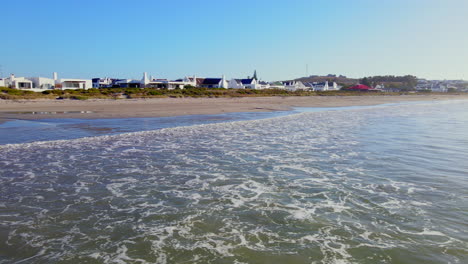 Low-aerial-view-over-gentle-waves-breaking-on-sandy-beach-in-Paternoster