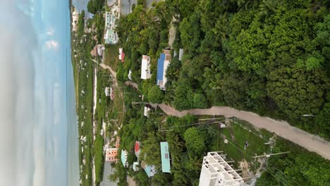 Drone-portrait-view-in-Belize-flying-over-caribbean-sea,-a-caye-covered-with-palm-trees-and-restaurants-on-a-cloudy-day