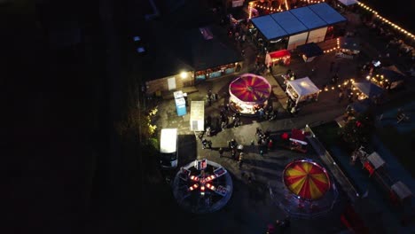 Illuminated-Christmas-funfair-attraction-in-neighbourhood-car-park-at-night-aerial-view