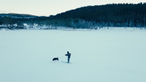 Mann-Auf-Ski,-Gezogen-Von-Einem-Hund-Auf-Einem-Zugefrorenen-See-Im-Winter
