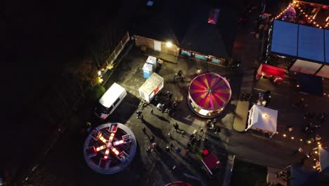 Illuminated-Christmas-spinning-fairground-rides-in-neighbourhood-pub-car-park-at-night-aerial-view