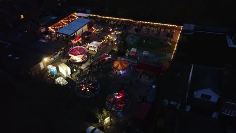 Illuminated-Christmas-fairground-festival-in-neighbourhood-pub-car-park-at-night-aerial-view