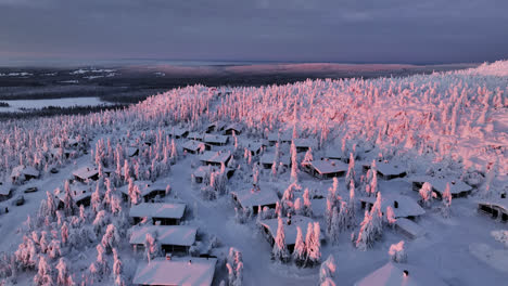 Aerial-overview-of-snowy-lodges-on-a-mountain-summit,-pink-morning-in-Lapland