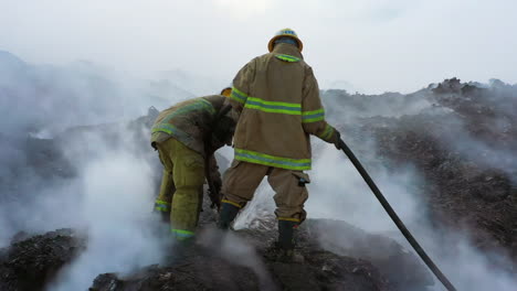 Two-Firefighters-fighting-a-wildfire,-on-smoky-ground,-cloudy-day,-in-Dominican-Republic